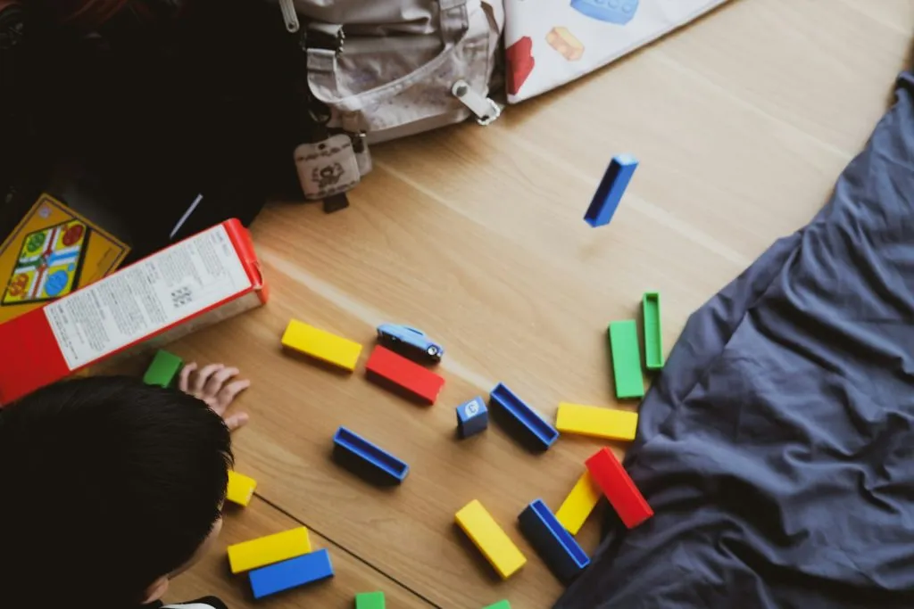 Child playing with colorful building blocks on a wooden floor, the kind of play-based learning used in both clinic-based and in-home ABA therapy