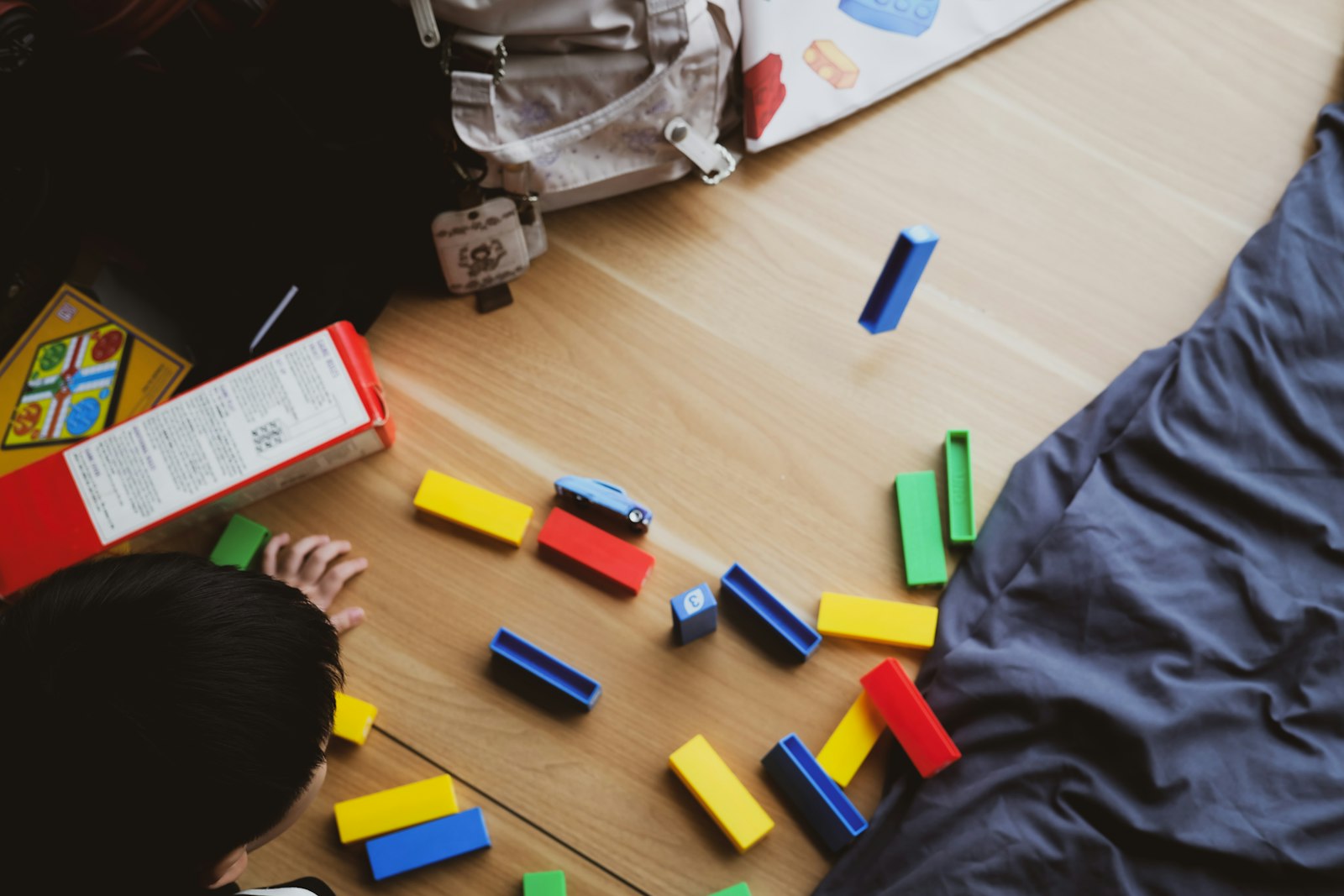 Child playing with colorful building blocks on a wooden floor, the kind of play-based learning used in both clinic-based and in-home ABA therapy